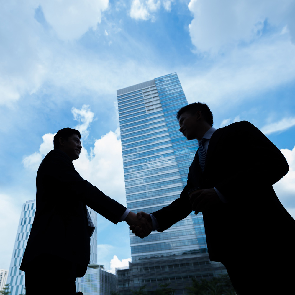 Two Business People Shaking Hands in front of tall building