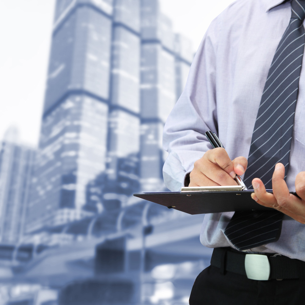Man writing on clipboard in front of tall buildings
